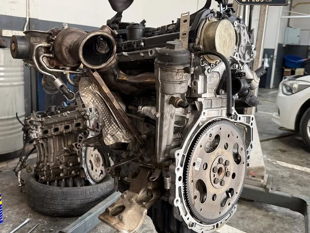 เครื่องยนต์ BMW ที่ยกลงมาจากรถทั้งลูกวางบนแท่น เห็นเทอร์โบ ท่อร่วมไอเสีย และฟลายวีล ระหว่างงานซ่อมใหญ่ที่อู่ P-Plus BM Service